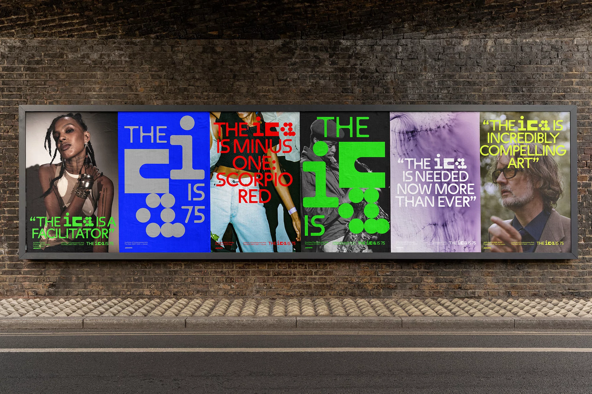 Large billboard featuring diverse art posters with typography and portraiture, set against a brick wall on a city street.