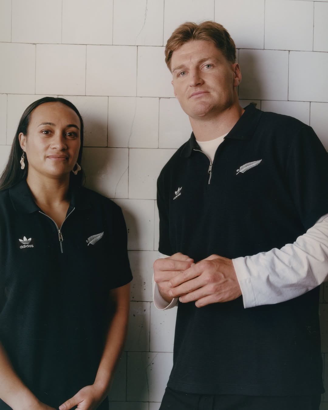 Portrait of a man and a woman in black athletic wear standing side-by-side in front of a tiled wall with neutral facial expressions.