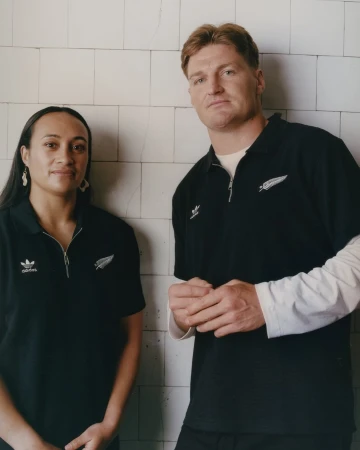 Portrait of a man and a woman in black athletic wear standing side-by-side in front of a tiled wall with neutral facial expressions.