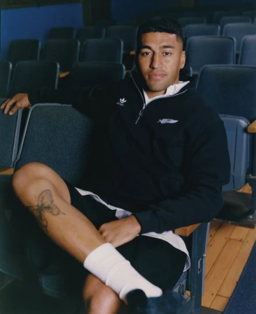 Portrait of adult male wearing Adidas sweatshirt, sitting on a blue chair in an auditorium with rows of empty seats in the background.