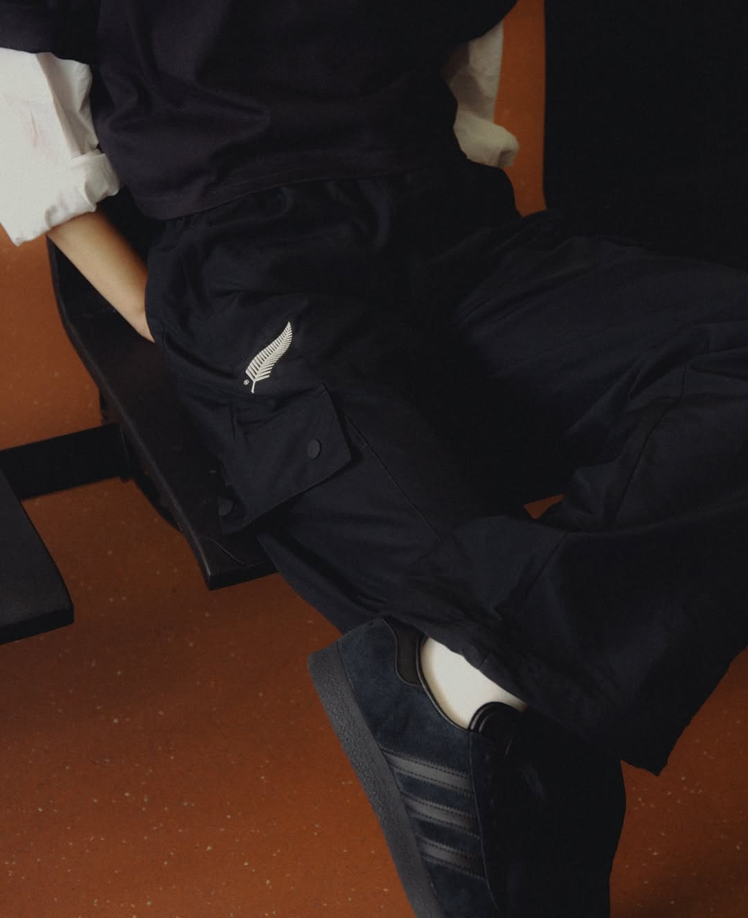 Fashionable person sits in an indoor setting wearing dark pants and blue sneakers, showcasing street style.