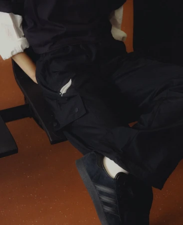Fashionable person sits in an indoor setting wearing dark pants and blue sneakers, showcasing street style.