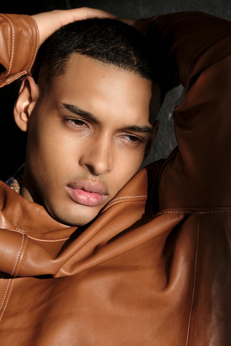 Close-up portrait of a handsome adult male model with dark hair and brown leather jacket in a photo studio with dramatic lighting.