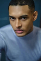 Close-up portrait of a young man wearing a light blue top against a dark blue background for L'Officiel Baltics.