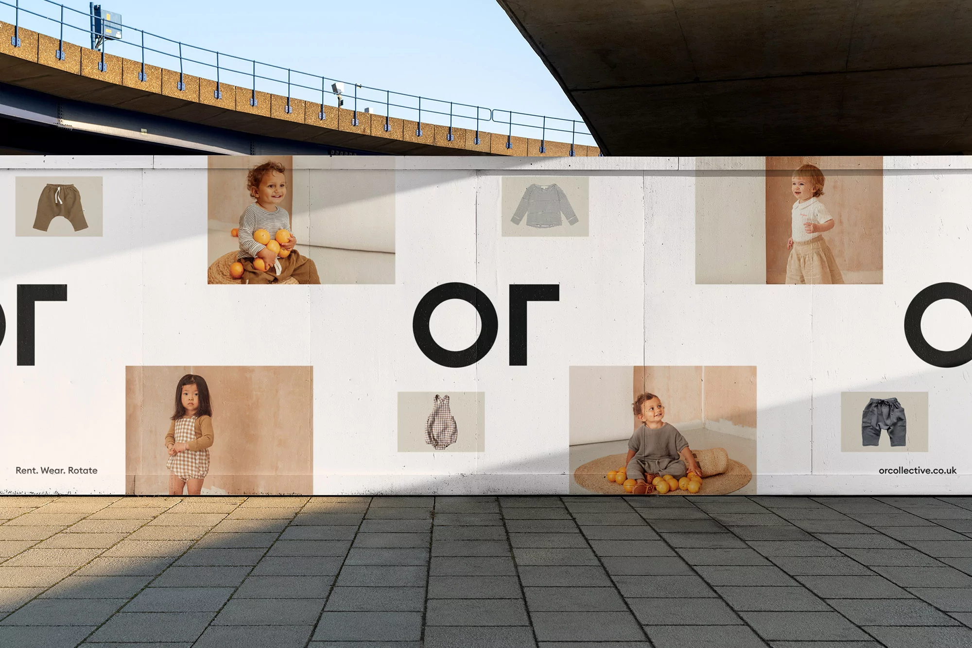 Outdoor advertisement featuring children's clothing with smiling toddlers and stylish outfits under a concrete bridge, promoting a brand.