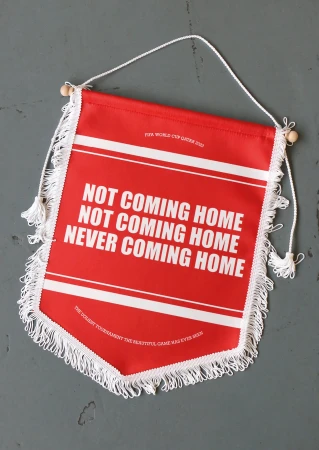 Red and white banner with a humorous slogan related to a soccer world cup, displayed indoors against a textured gray background.