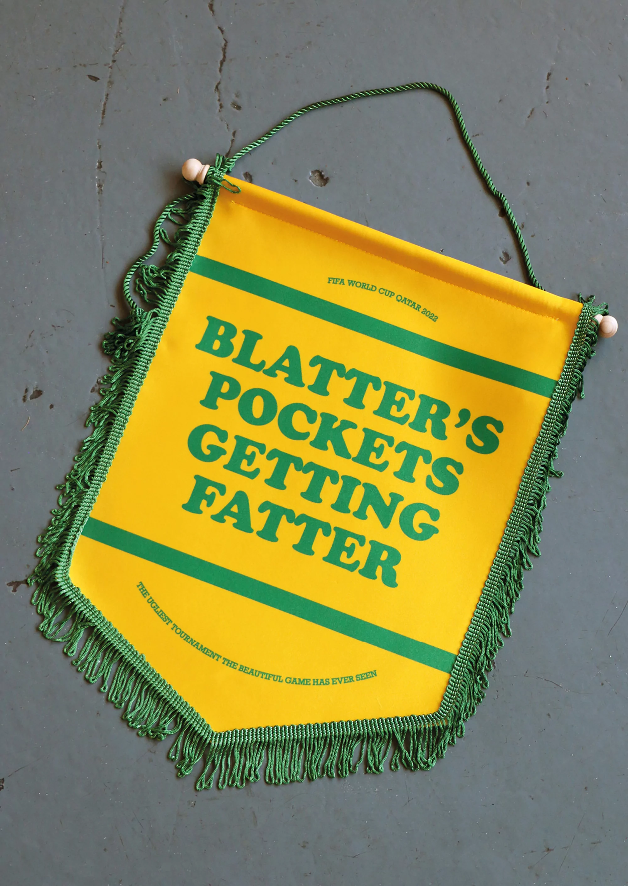 Yellow pennant with green fringe and green text displaying a political slogan about FIFA and the 2022 World Cup in Qatar.