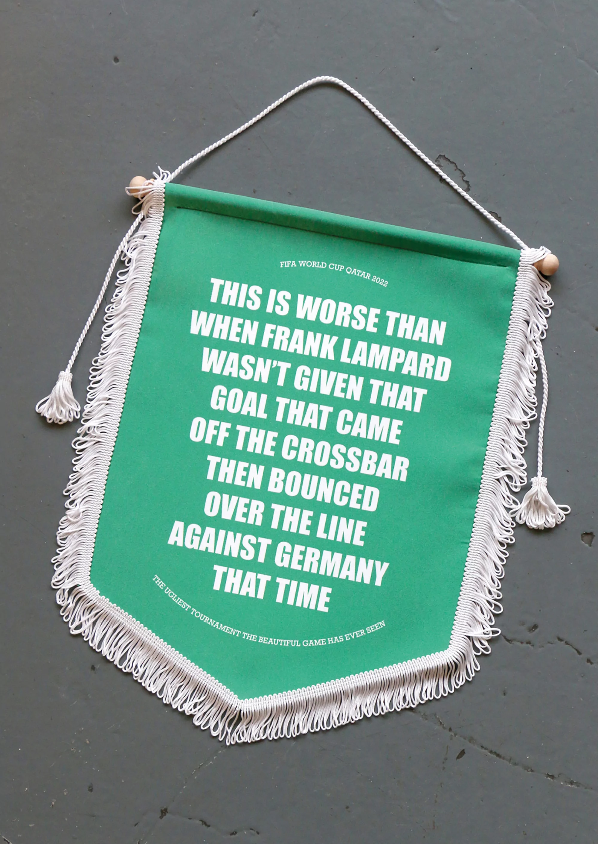 Close-up of a green and white banner with text about a soccer goal, featuring a fringed edge and hung by a white rope.