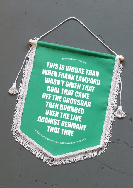 Close-up of a green and white banner with text about a soccer goal, featuring a fringed edge and hung by a white rope.