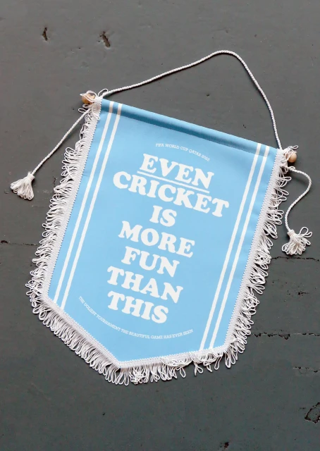 A blue and white pennant with the text 'EVEN CRICKET IS MORE FUN THAN THIS' hangs against a grey background, offering a humorous take.