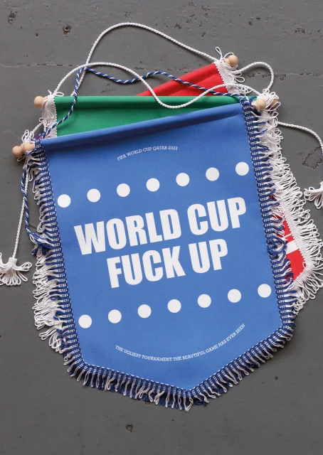 Three pennant banners in red, green, and blue with humorous white text and fringe details, hanging against a grey surface.