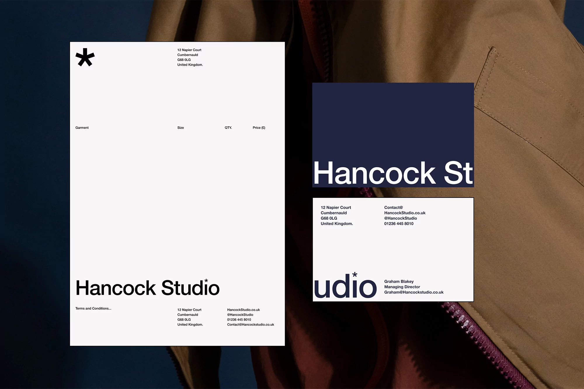 Promotional image displays Hancock Studio branding with business card and tan jacket detail against a blue-grey backdrop, clean and modern.