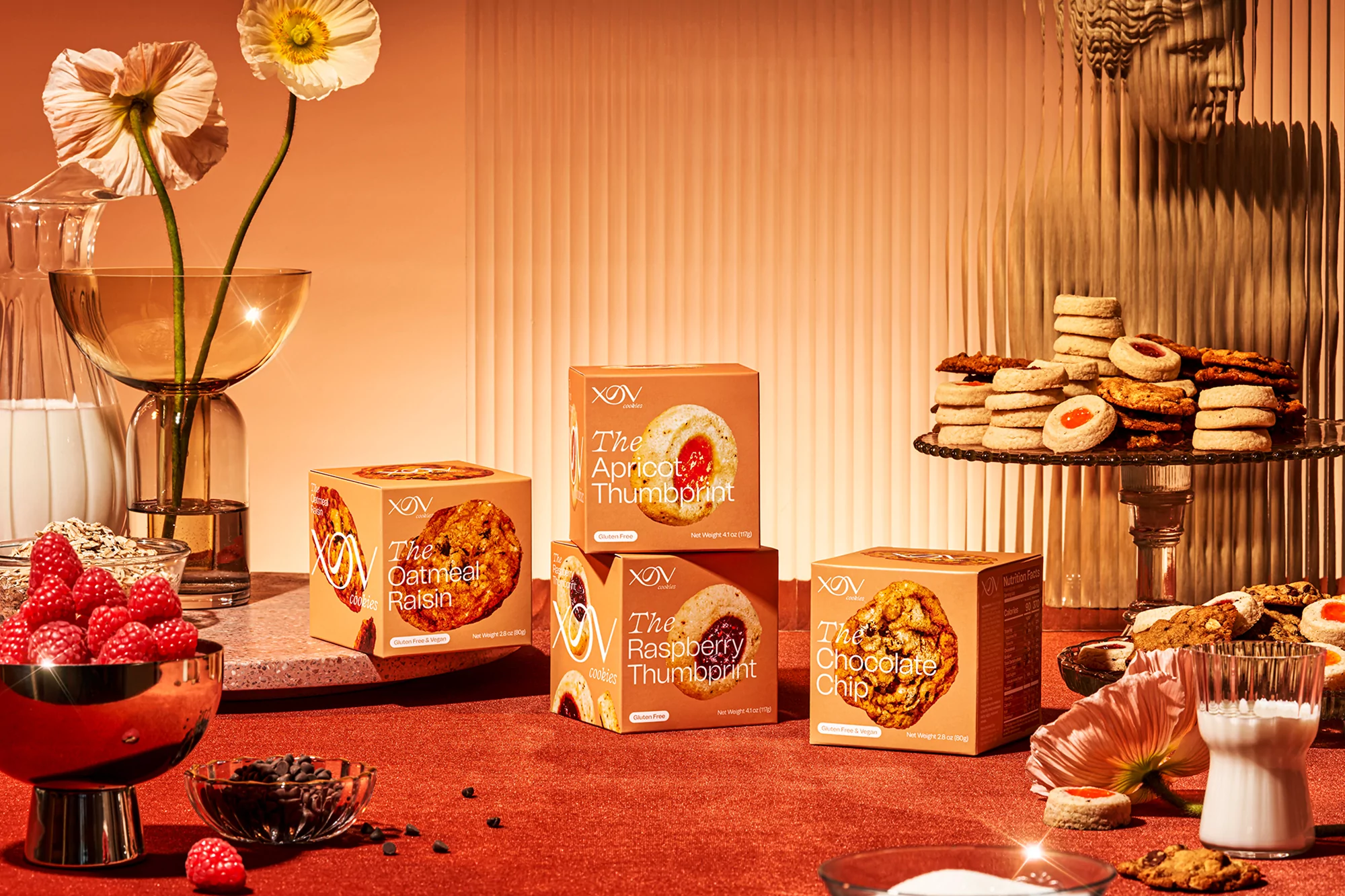 Cookie boxes arranged on a table with floral arrangements, dessert stands with cookies, and bowls of chocolate chips and berries.