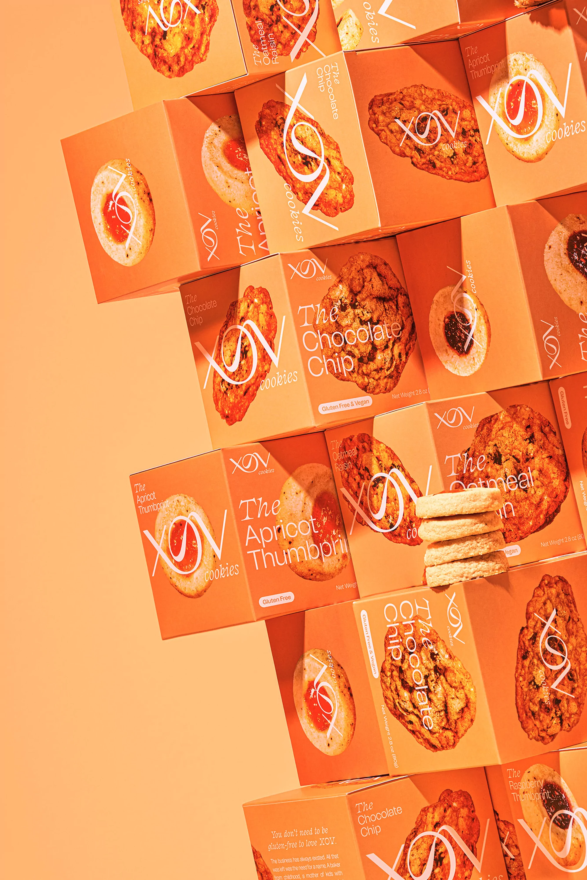 Stack of XOX Cookies brand boxes in apricot and white tones, some with cookies stacked near them, against a solid apricot background.
