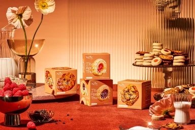 Commercial still life of XOV cookie packaging on a deep red surface with fresh raspberries, milk glasses, and classical statue decor.
