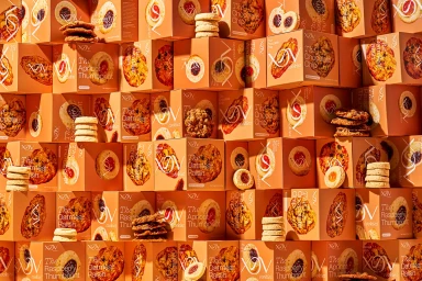 A textured arrangement of XOV cookie boxes stacked densely with photographs of cookies and stacks of actual baked cookies.