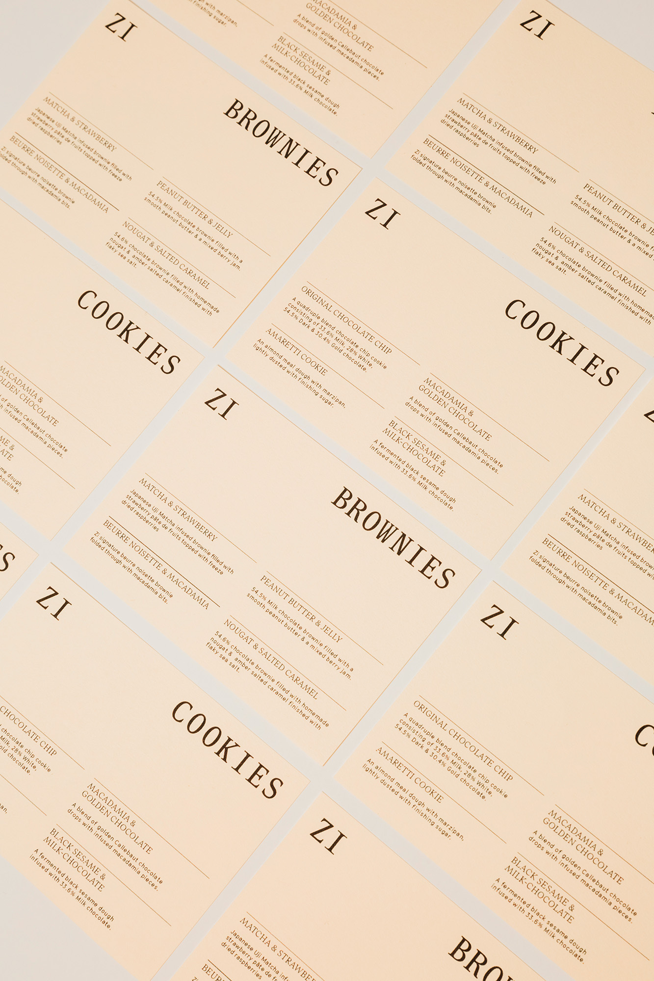 Arrangement of printed sheets displaying menus for cookies and brownies with product descriptions and brand logo on a neutral surface.