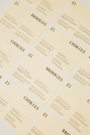 Minimalist cream packaging labels with black serif typography arranged in a repeating pattern on a light surface.