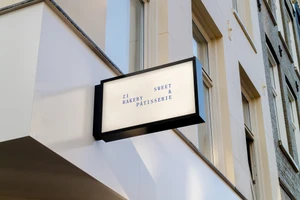 Rectangular backlit storefront sign featuring blue typographic branding mounted on a light-colored building exterior