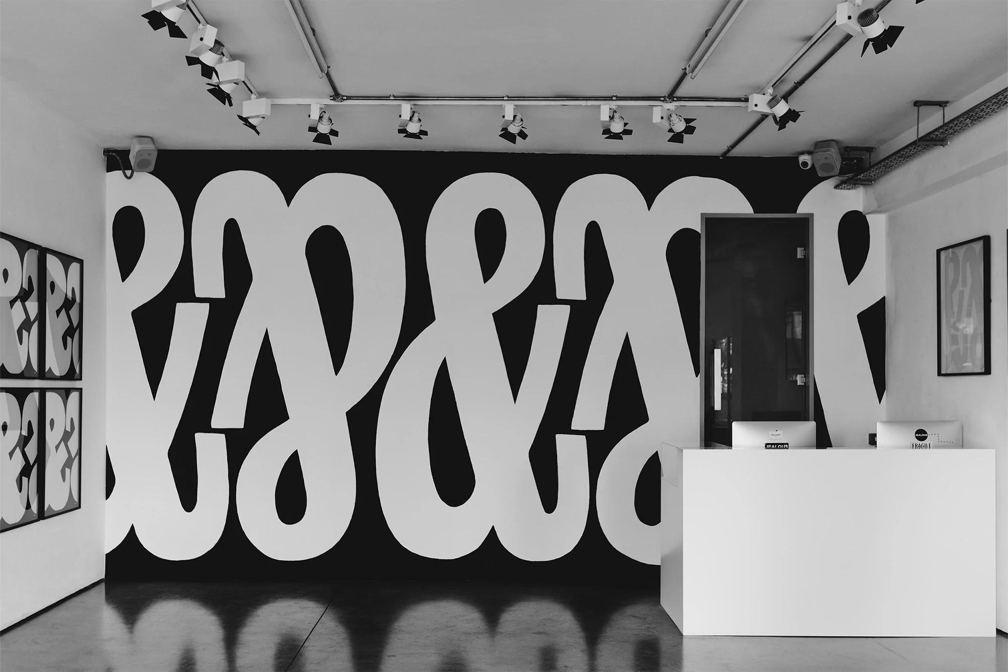 Interior view of a room with a large black and white graphic wall art, complemented by a white reception desk and track lighting.