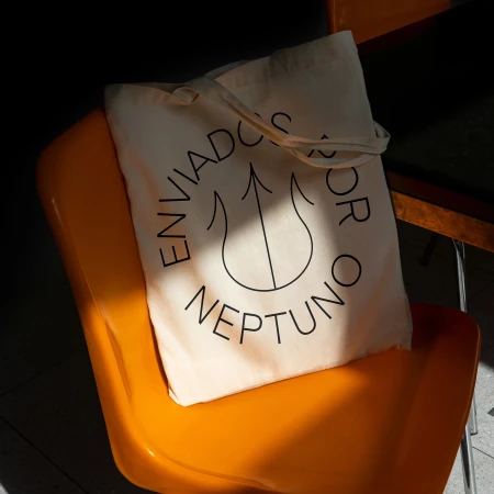 Beige tote bag on orange chair with black text design and minimalist line art in contrasting light and shadows; modern design.