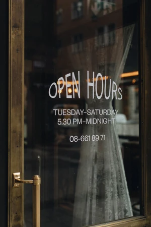 Glass restaurant door with open hours text and brass handle featuring interior view and dress