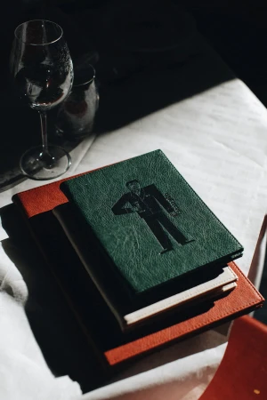 Stacked leather-bound notebooks and a wine glass on a white tablecloth under directional lighting for Italiano.