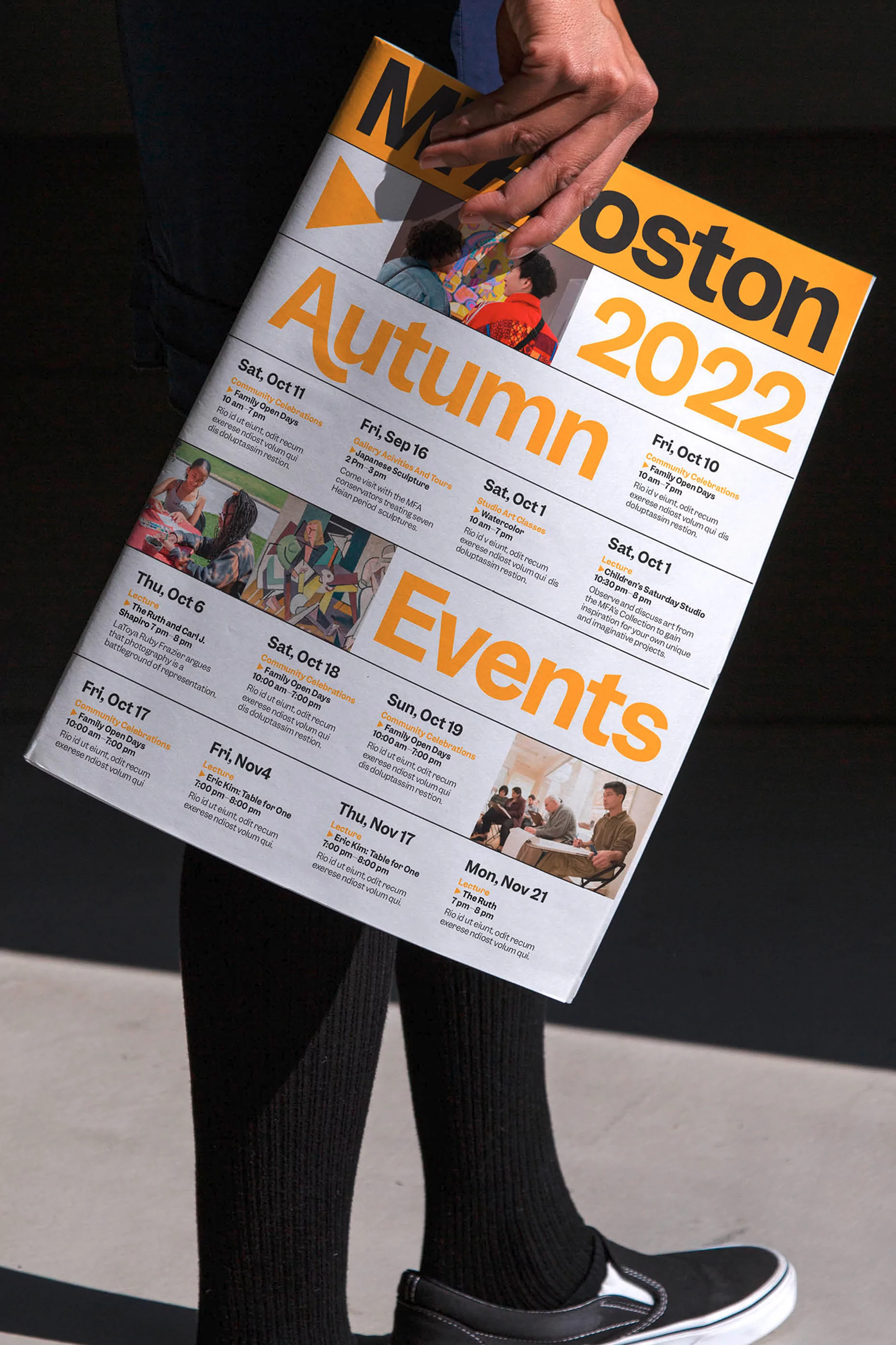 Person holding a 'Moston Autumn Events 2022' magazine with dates and activities, wearing black socks and slip-on shoes.
