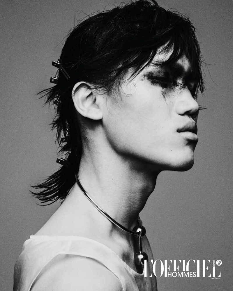 Black and white portrait of a young Asian adult male with dark hair and smeared makeup, wearing a silver necklace and white top.