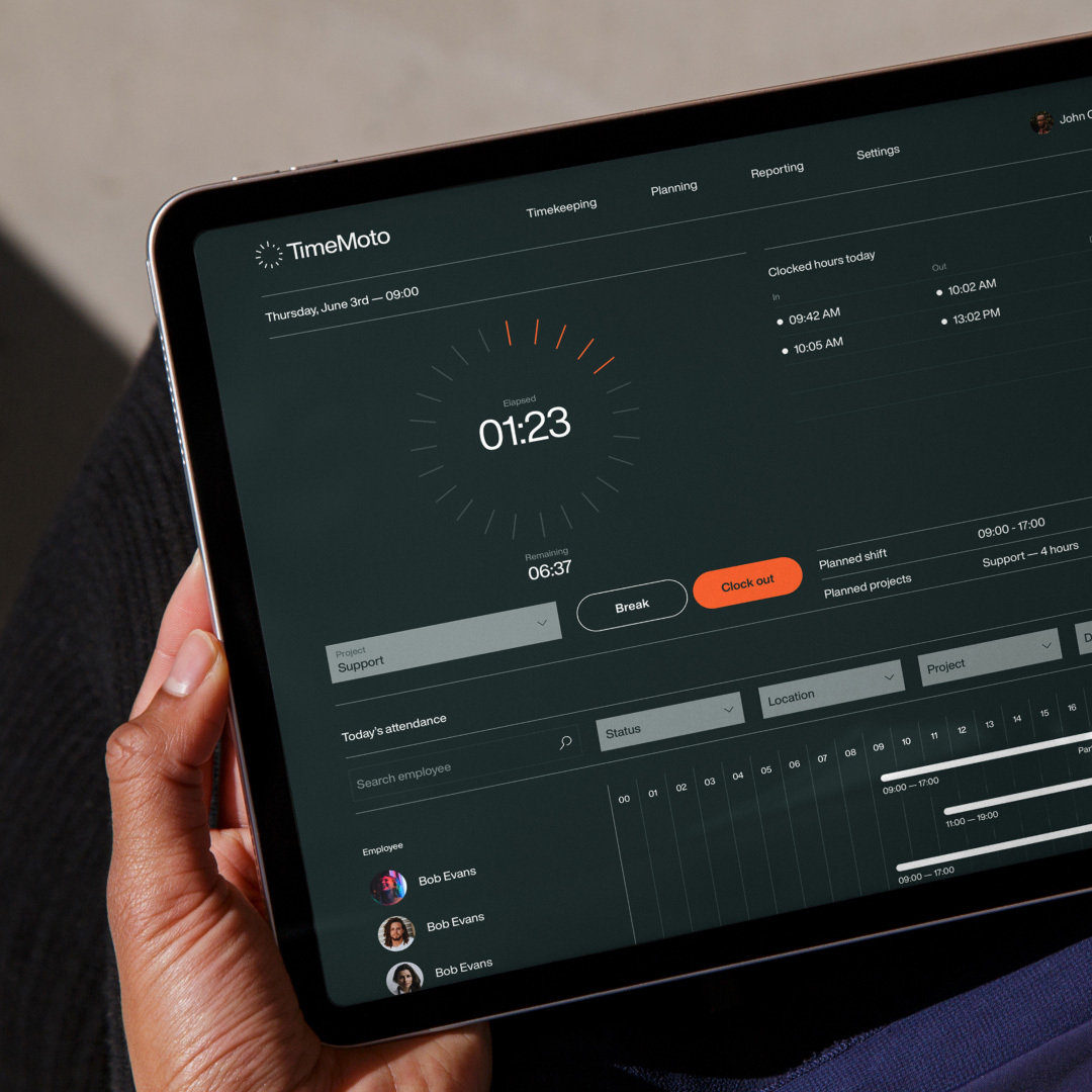 Close-up of a person holding a tablet displaying timekeeping software, showing a digital clock and employee attendance information.