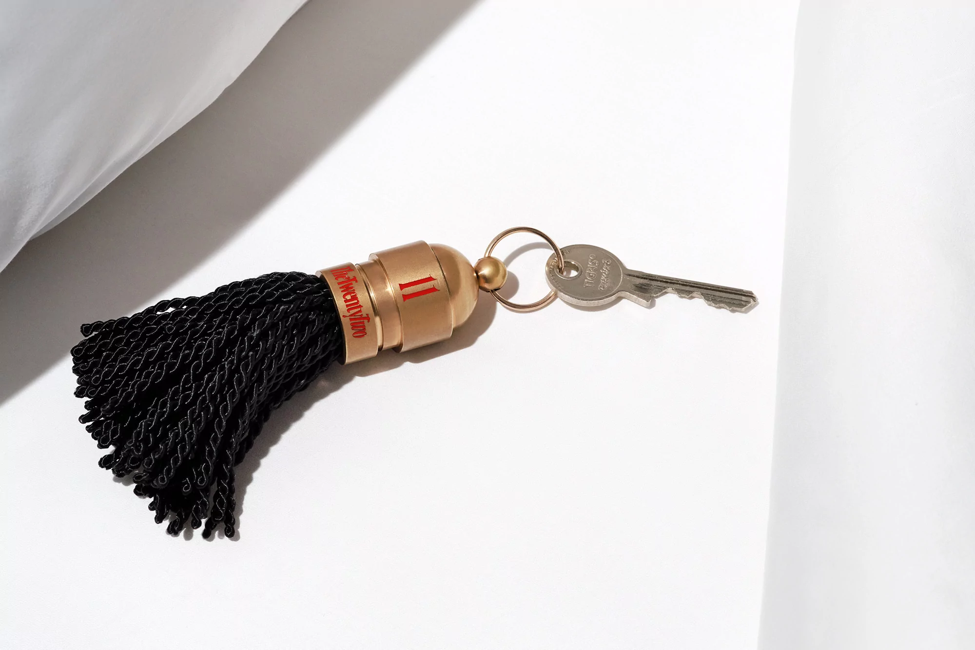 Hotel room key with black tassel against a white background, lit from above, product shot, clean minimalist composition.