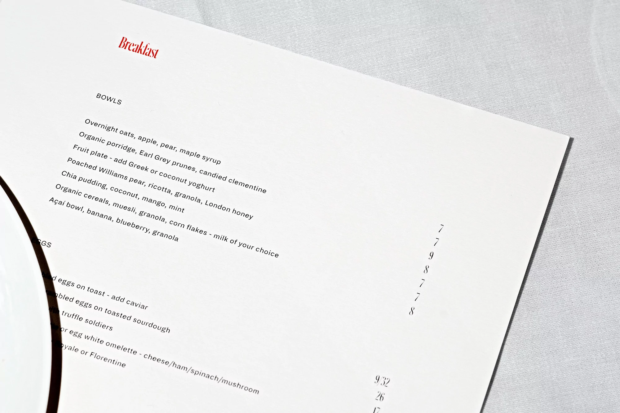 Close-up of a breakfast menu featuring a selection of bowls including overnight oats, chia pudding, and an açai bowl on a white tablecloth.