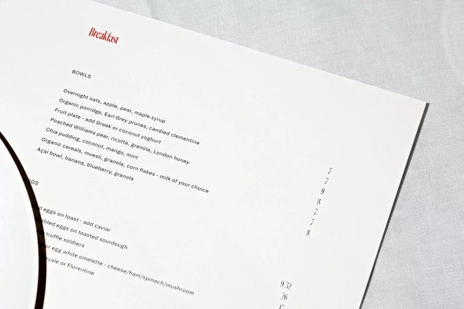 Close-up of a breakfast menu featuring a selection of bowls including overnight oats, chia pudding, and an açai bowl on a white tablecloth.