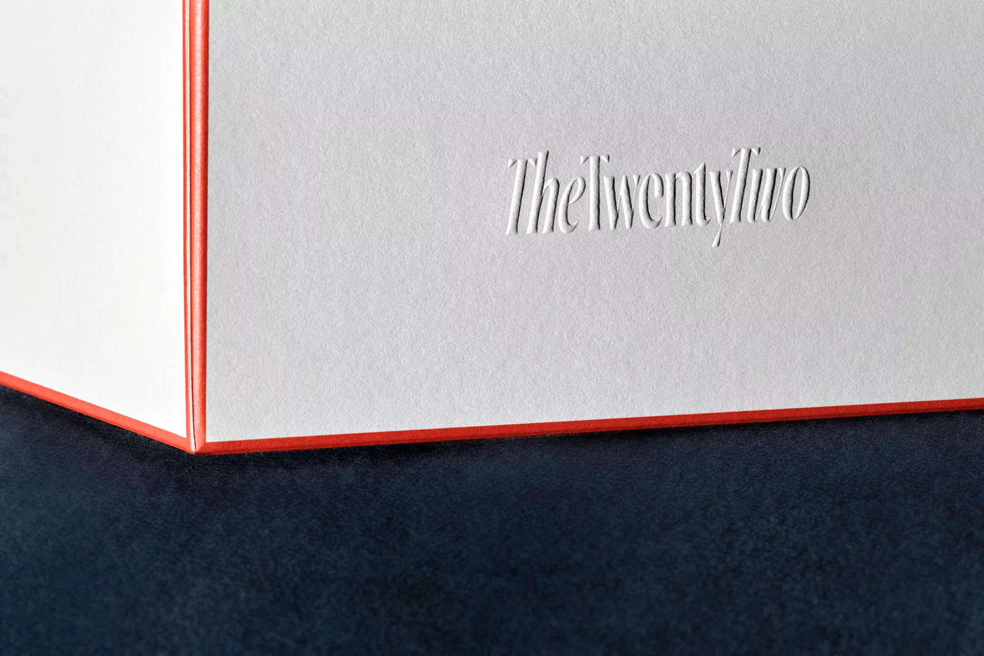 Close-up of a white box with orange trim and debossed text on a dark surface, emphasizing texture and minimalist design.