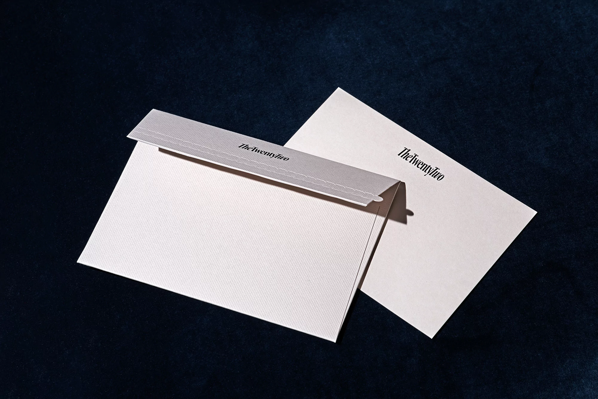 Close-up of a light pink envelope and matching paper against a dark blue background, showcasing the stationery branding.