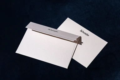 Cream textured envelope and stationery card with dark branding displayed on a dark velvet surface