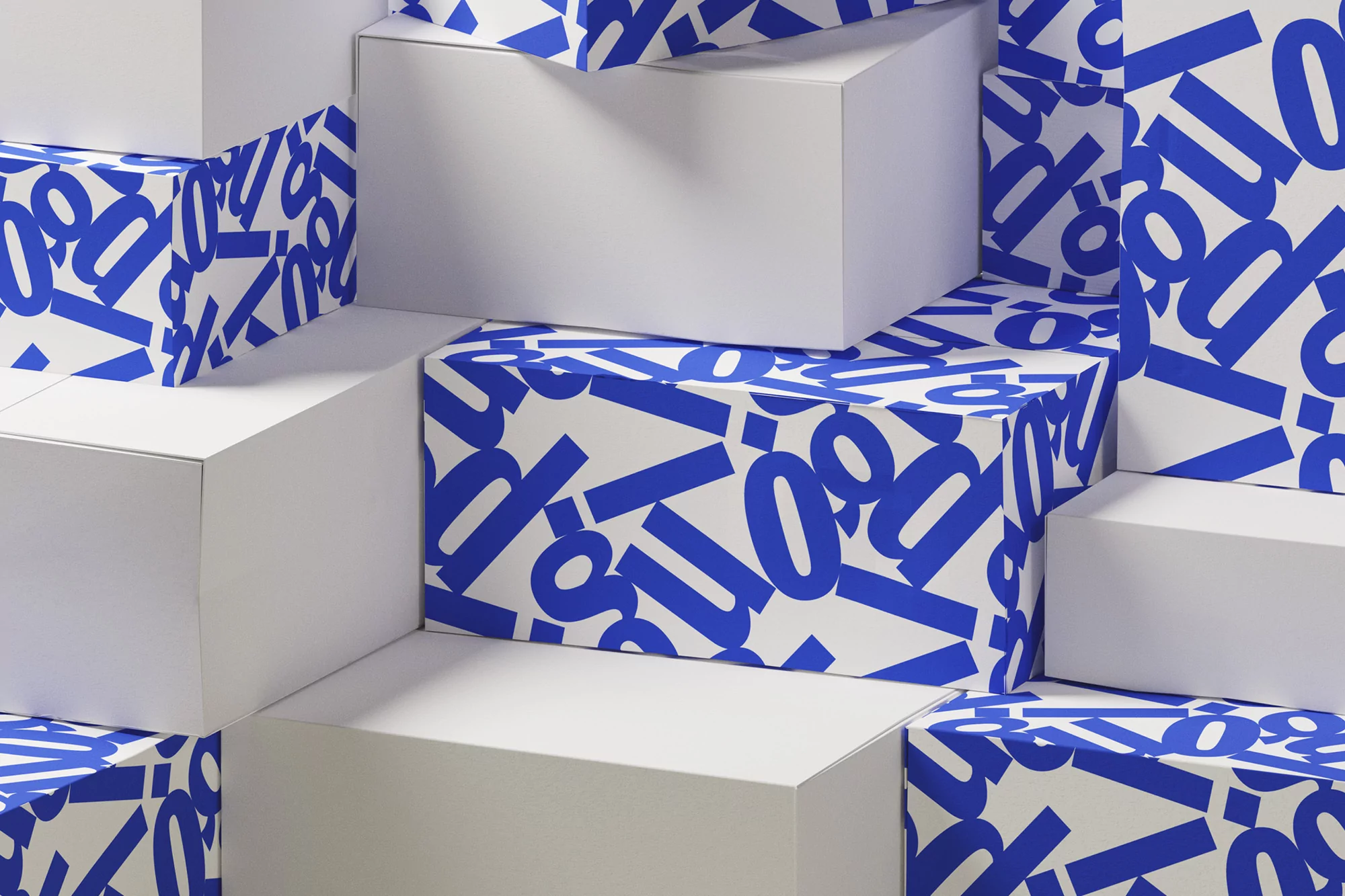 Stacked white boxes with a blue letter pattern create a geometric design, highlighting texture and three-dimensional form in an indoor setting.