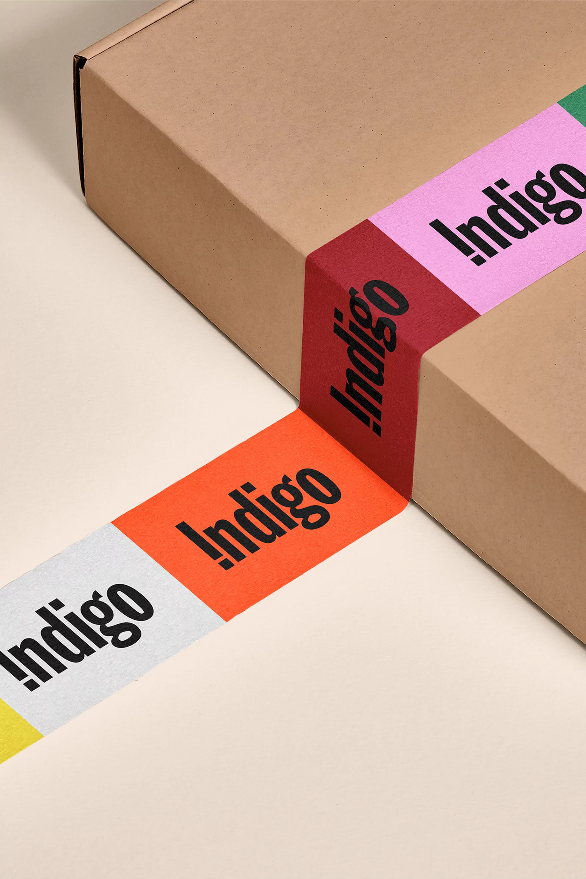 Close-up of a brown cardboard box sealed with a colorful tape featuring the word Indigo, set against a neutral beige background.