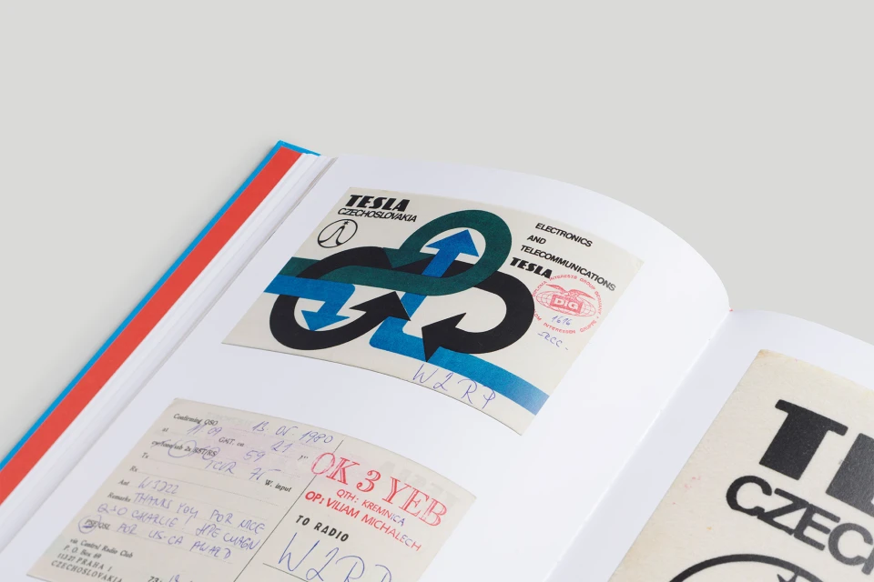Open book displays Tesla Czechoslovakia electronics logo with intertwined arrows on a white page, with surrounding text and handwriting.
