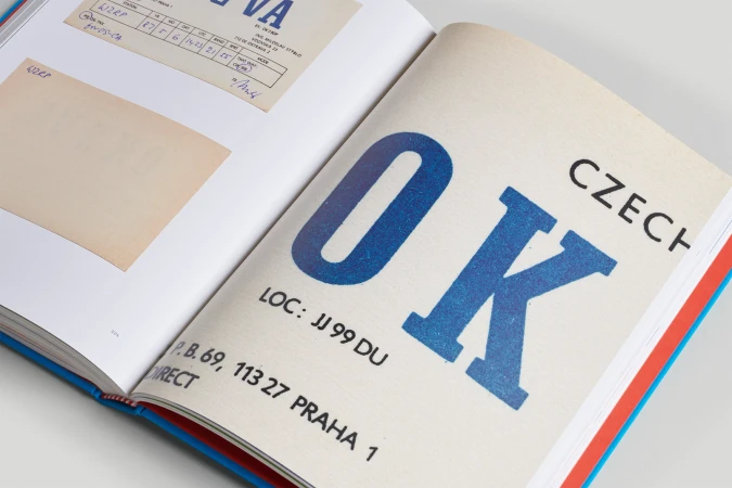 Open book displays blue 'OK CZECH' text on white page; additional sheets and text visible on the facing page.