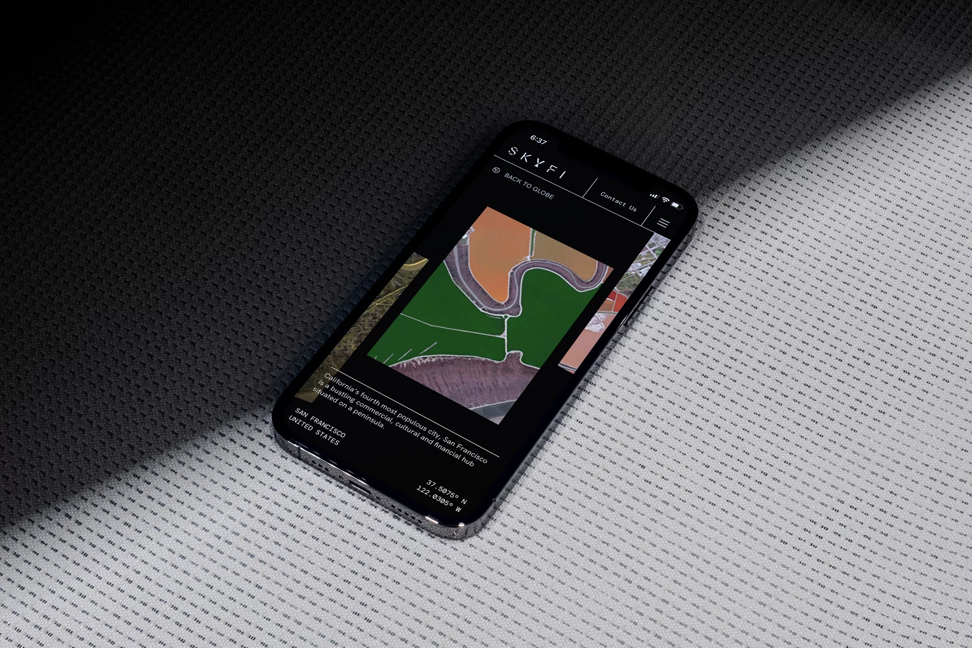 Mobile phone displaying the Skyfi website with aerial imagery and text about San Francisco, set on a textured dark and light surface.