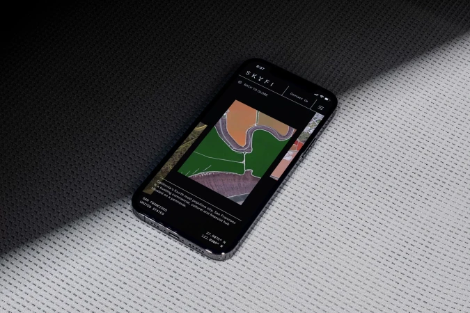 Mobile phone displaying the Skyfi website with aerial imagery and text about San Francisco, set on a textured dark and light surface.