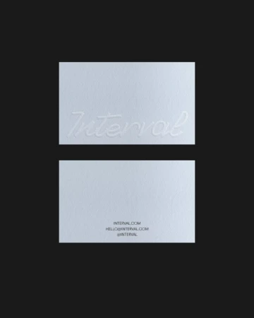 Two white textured business cards with debossed script typography displayed against a solid dark grey background.