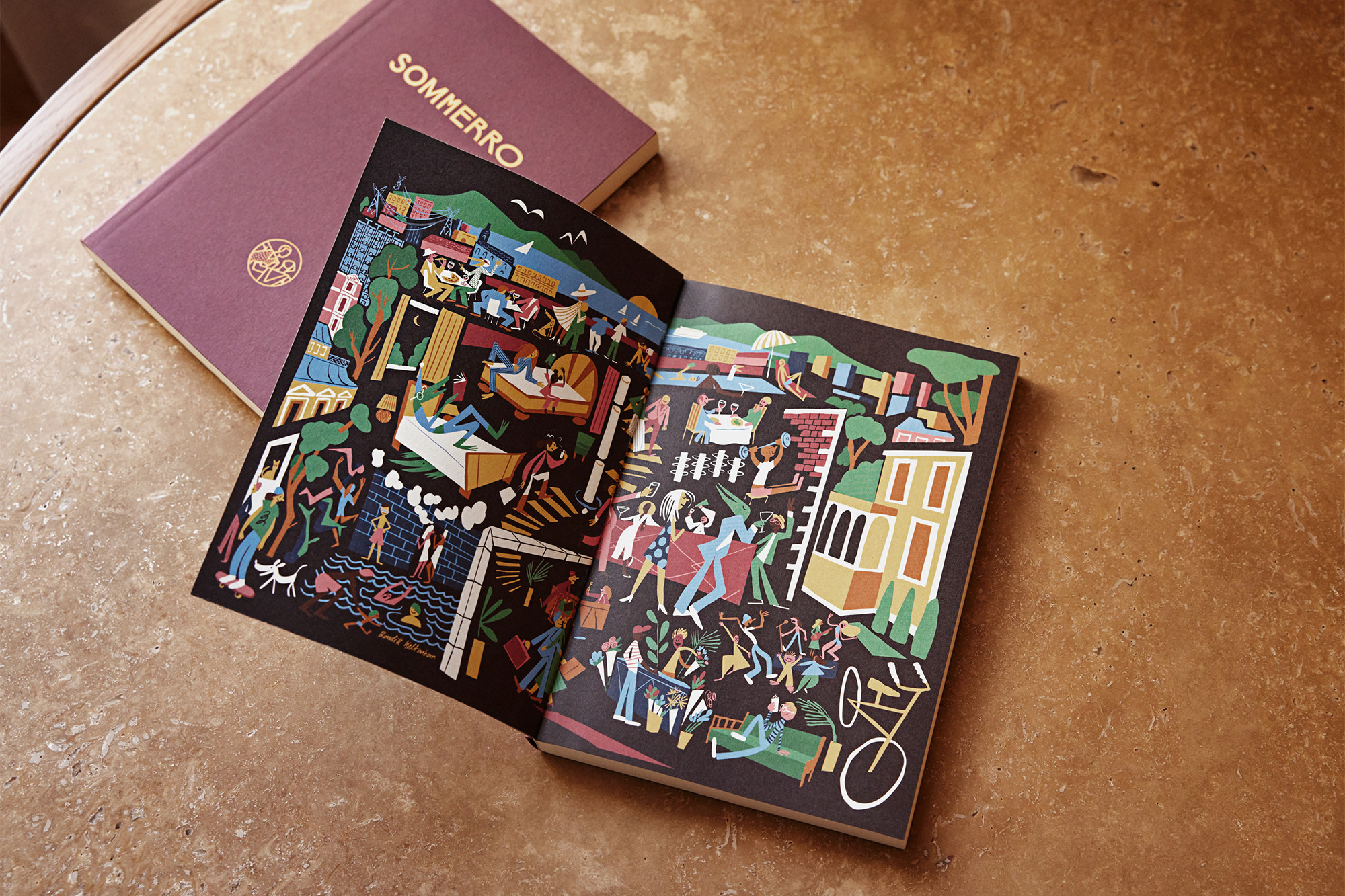 Illustration in an open book, showing colorful town scenes with people and buildings, next to a closed book on a brown textured surface.