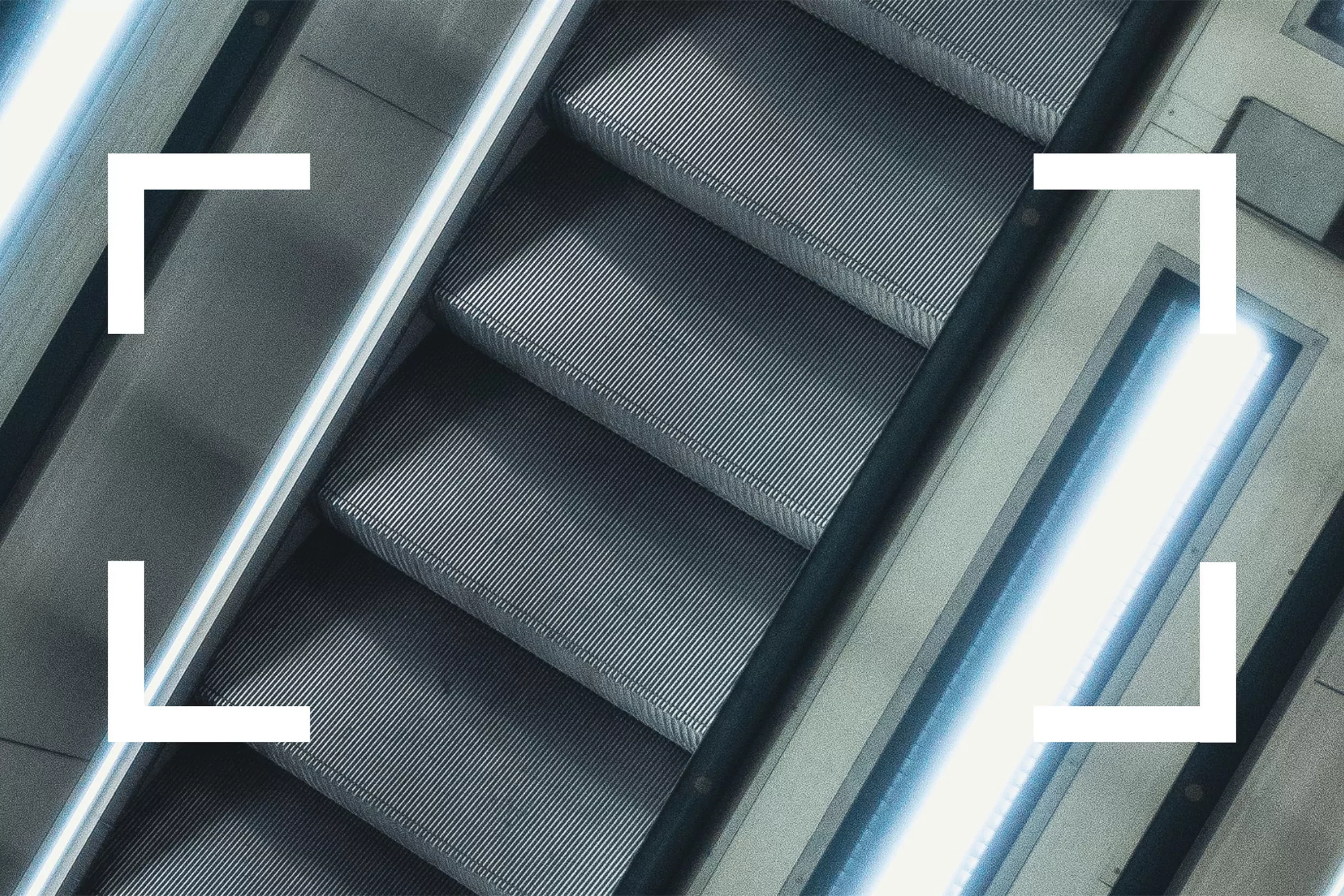 Abstract shot of escalator steps with illuminated side panels, viewed from above at an angle, in cool grays and blues.