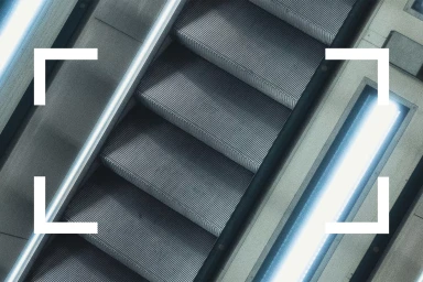 High angle shot of a moving escalator with bright illuminated handrails and white framing crop marks overlay.