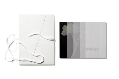 White textured folder with white ribbon and a booklet featuring layered translucent pages against a plain white background.