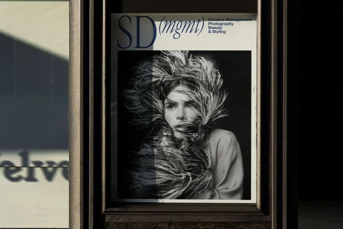 Black-and-white image of a magazine cover displayed in a window. The cover features a person with feathered adornments around their head.