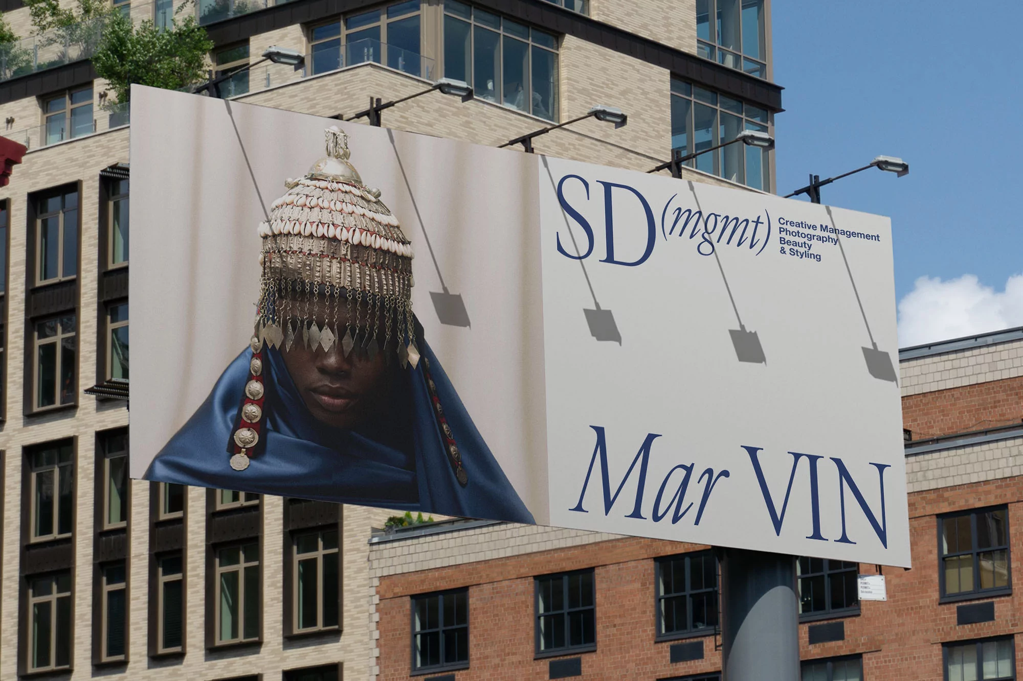 Outdoor billboard featuring a close-up shot of a model wearing a headdress and blue shawl, with building facades in the background.