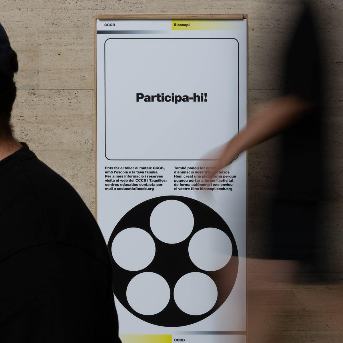 A person walks past an advertisement for a CCCB workshop, featuring bold typography and graphic elements on a white background.